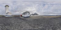 this is a photo of a lighthouse with clouds in the background and a house on the left and a small white building with a red door