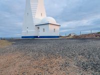 a lighthouse with a blue roof and a white chimney on top of gravel ground near the ocean