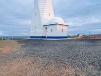 a lighthouse with a blue roof and a white chimney on top of gravel ground near the ocean