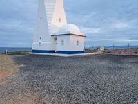 a lighthouse with a blue roof and a white chimney on top of gravel ground near the ocean