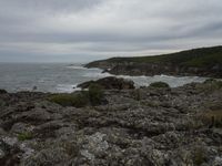 the man is standing near the ocean on the rocks next to the water, and one person is para sailing