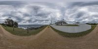 a person riding a skateboard down a dirt road under a cloudy sky with sea and white houses behind it