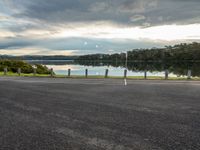 the road looks straight ahead, along with some trees by the water and the grass is on the side