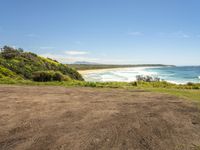 a graveled area with an ocean view next to the grass covered beach area and blue sky