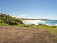 a graveled area with an ocean view next to the grass covered beach area and blue sky