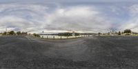 fish eye view of a wide open roadway with a lake and city behind it from a convex image