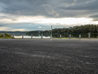 a woman running across a road near a lake in the background and poles and trees