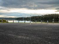 a woman running across a road near a lake in the background and poles and trees