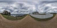 a person riding a skateboard down a dirt road under a cloudy sky with sea and white houses behind it