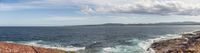 the ocean and the cliffs in the distance is blue with white clouds above it at the top