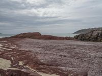 a red and brown beach next to a body of water and a mountain in the distance