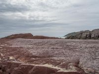 a red and brown beach next to a body of water and a mountain in the distance