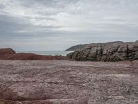 a red and brown beach next to a body of water and a mountain in the distance