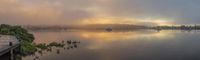 boats float in the water while a cloud hangs over the shore of a lake, in the afternoon sun