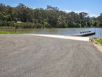 the water is reflecting the sky and treetops behind it, and a small boat ramp is in the middle of the road