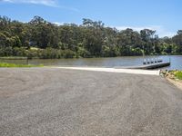 the water is reflecting the sky and treetops behind it, and a small boat ramp is in the middle of the road