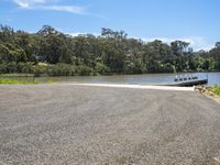 the water is reflecting the sky and treetops behind it, and a small boat ramp is in the middle of the road