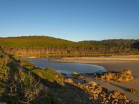 the sandy shore is lined with rocky boulders and trees along side it with a large lake behind it