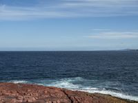 a person standing on some rocks with the ocean in the background of them and two birds flying over