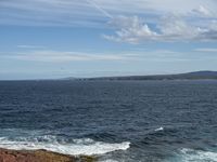 a person standing on some rocks with the ocean in the background of them and two birds flying over