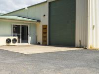 a small air conditioning unit in front of a building with a large open door and metal doors