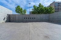 the empty parking lot in front of a wall with apartment buildings on it and a skateboarder on a ramp