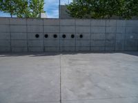 the empty parking lot in front of a wall with apartment buildings on it and a skateboarder on a ramp