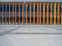 a concrete structure made into rows of orange and yellow poles are on a cement sidewalk