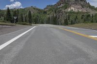 the asphalt road is in between two parallel lanes surrounded by forested forests and mountains in the distance