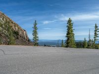 the curved road is near an evergreen mountain side area with rocks and trees in winter