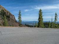 the curved road is near an evergreen mountain side area with rocks and trees in winter