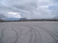 a paved parking lot with cloudy skies and mountain behind it, in the foreground is a mountain range