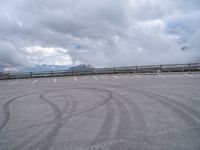 a paved parking lot with cloudy skies and mountain behind it, in the foreground is a mountain range