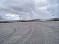 a paved parking lot with cloudy skies and mountain behind it, in the foreground is a mountain range