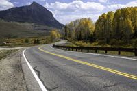 the mountain and forest along the highway have yellow foliage on the trees above them and the road is curved into the opposite direction