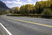 the mountain and forest along the highway have yellow foliage on the trees above them and the road is curved into the opposite direction