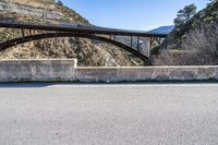 the person is riding their bike over the bridge at the foot of mountains in a scenic area