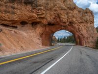 a large tunnel with some rocks in the background, a road running under it and a bridge between it