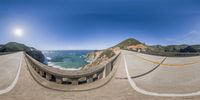 a 360 - view lens of a scenic ocean view with a bridge, and some cliffs