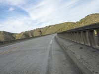 a motorcycle is driving along an empty highway on a clear day in the mountains and hills