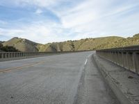 a motorcycle is driving along an empty highway on a clear day in the mountains and hills