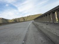 a motorcycle is driving along an empty highway on a clear day in the mountains and hills