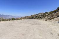 a dirt road in the hills between mountains and valleys is seen here with a clear blue sky