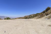 a dirt road in the hills between mountains and valleys is seen here with a clear blue sky