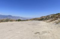 a dirt road in the hills between mountains and valleys is seen here with a clear blue sky