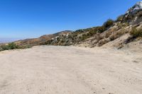 a dirt road in the hills between mountains and valleys is seen here with a clear blue sky