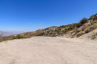 a dirt road in the hills between mountains and valleys is seen here with a clear blue sky