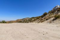 a dirt road in the hills between mountains and valleys is seen here with a clear blue sky