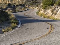 the curved road has two yellow lines on it near the mountain and the hills behind