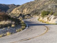 the curved road has two yellow lines on it near the mountain and the hills behind